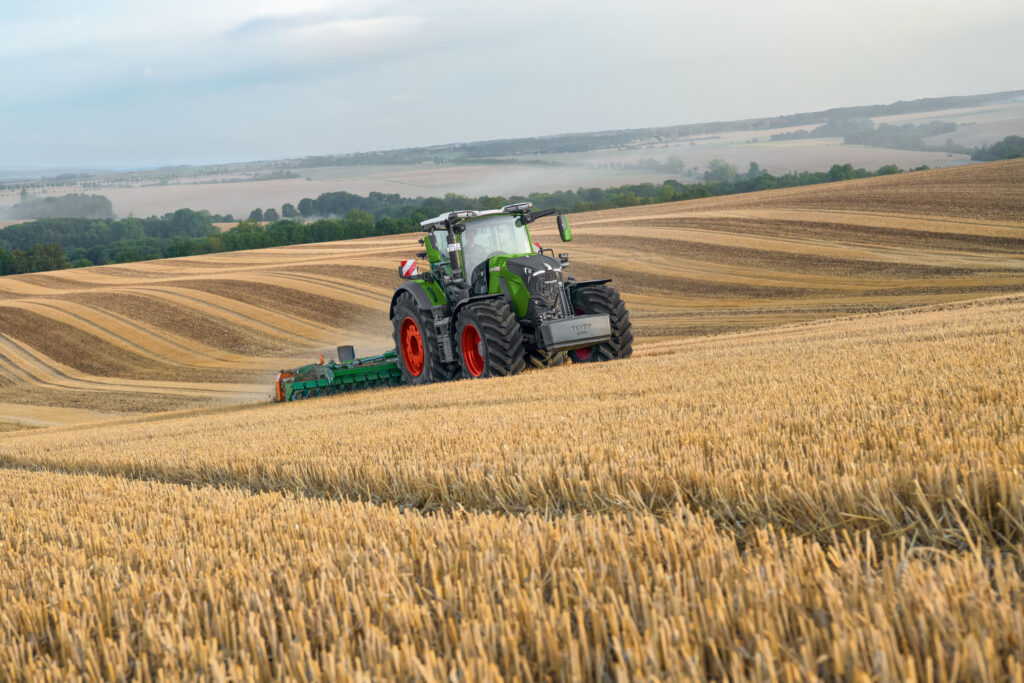 Fendt tractor with tillage implement working across rolling harvested grain fields